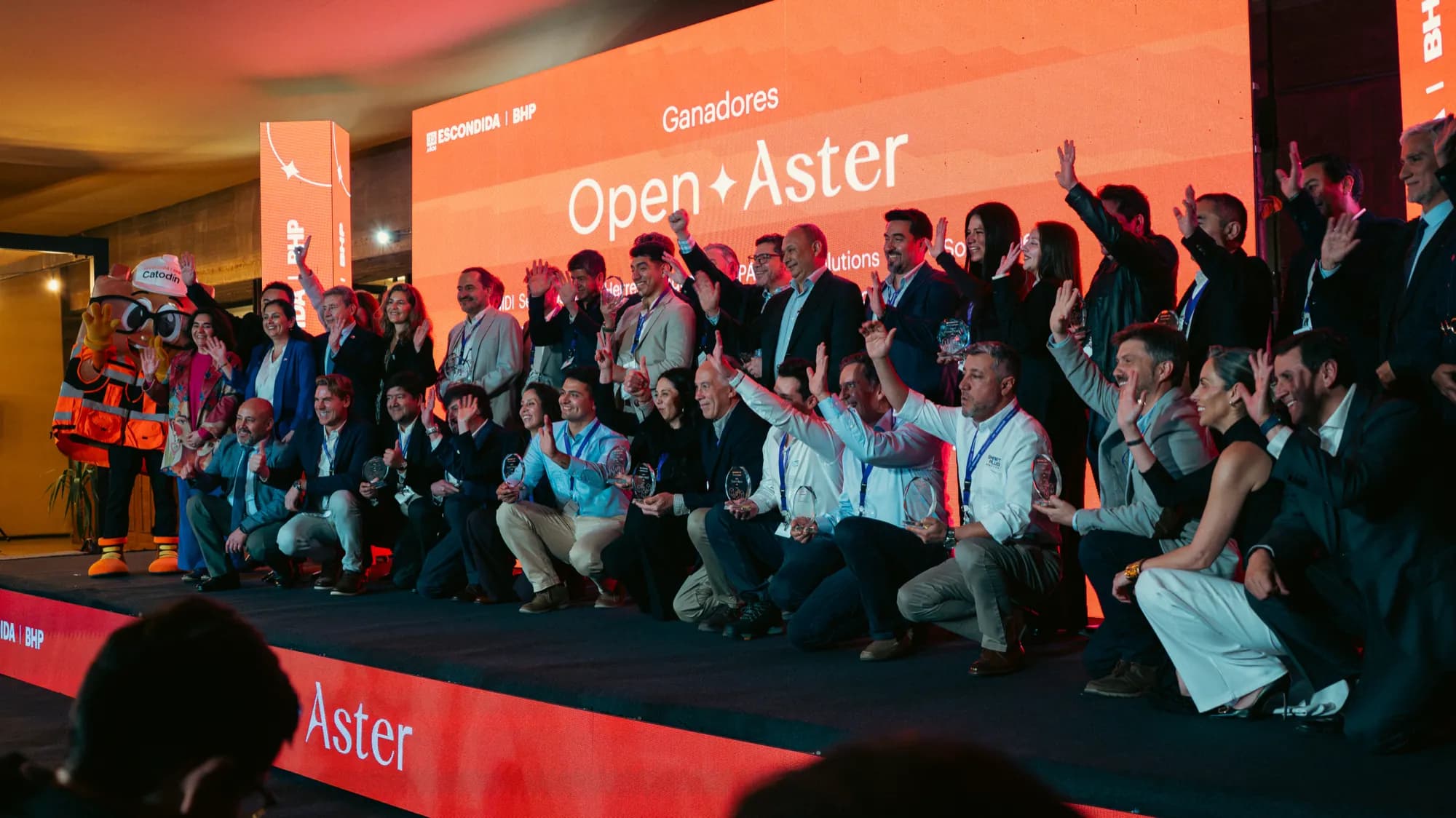 The companies selected for Open Aster on stage, holding their awards, with the Escondida | BHP screen behind them